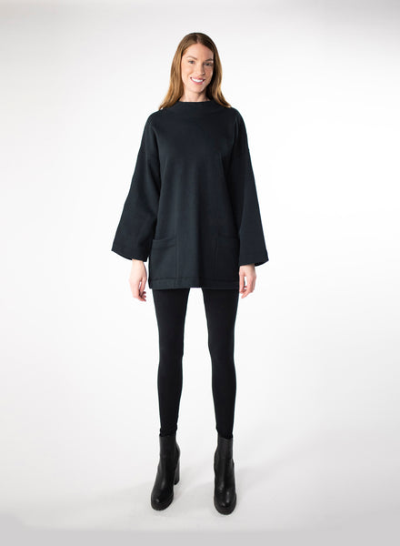 Black Organic Cotton Fleece tunic length sweater with full sleeves. Features front pockets and wide collar. Styled with black leggings