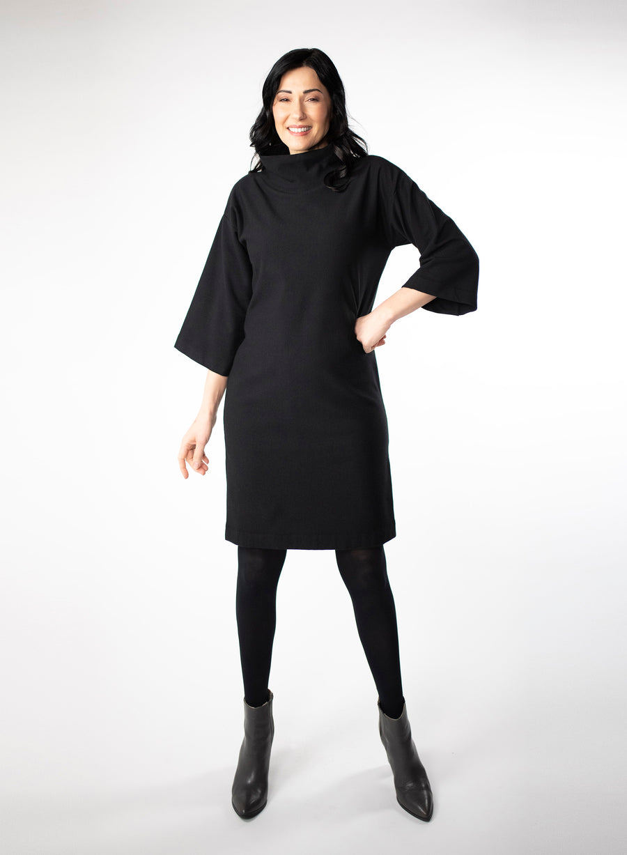 Black knee length Bamboo fleece sweater dress with full sleeves and wide mock neck collar. Styled with black leggings.