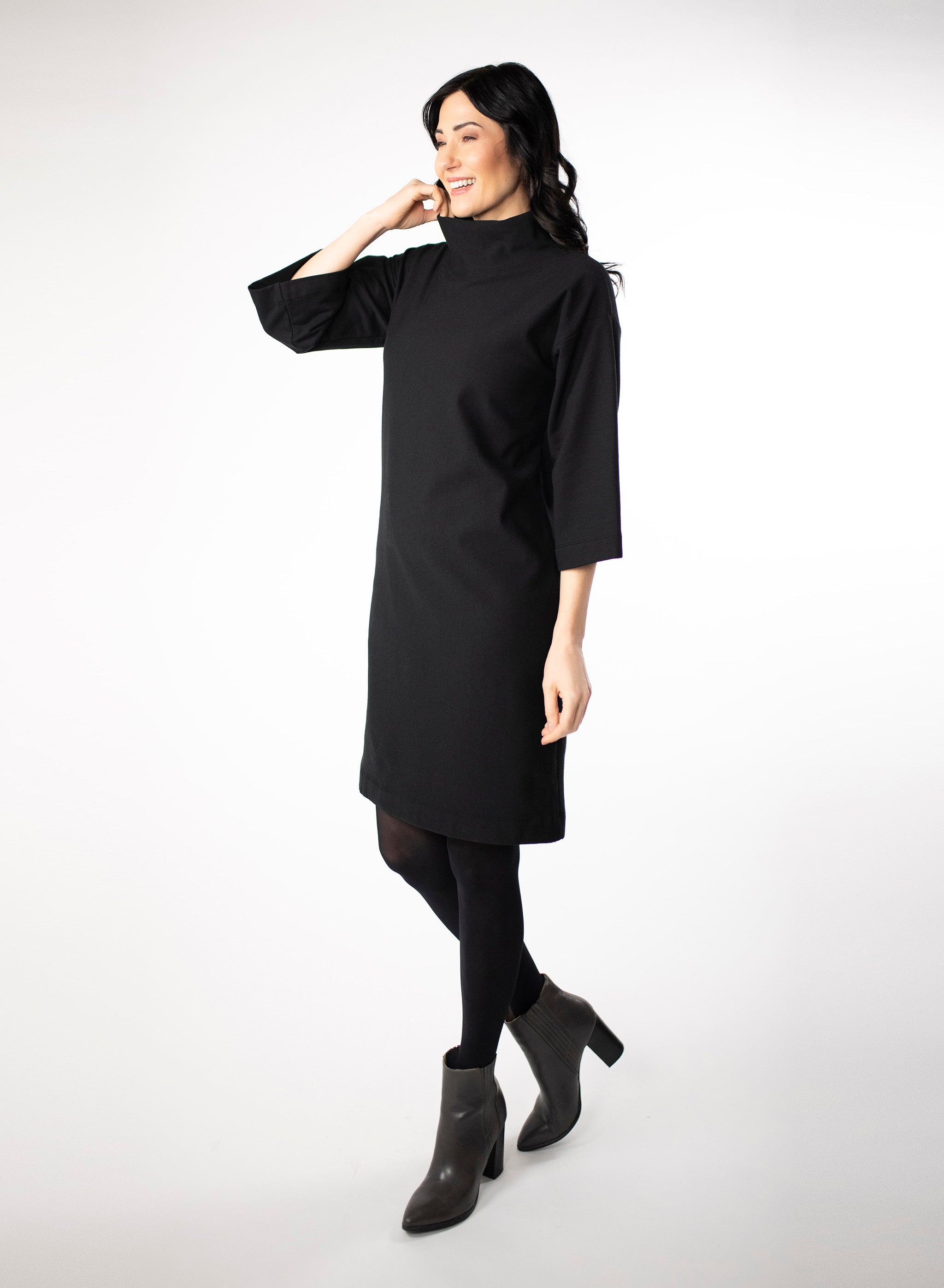 Black knee length Bamboo fleece sweater dress with full sleeves and wide mock neck collar. Styled with black leggings.