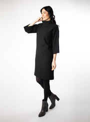Black knee length Bamboo fleece sweater dress with full sleeves and wide mock neck collar. Styled with black leggings.