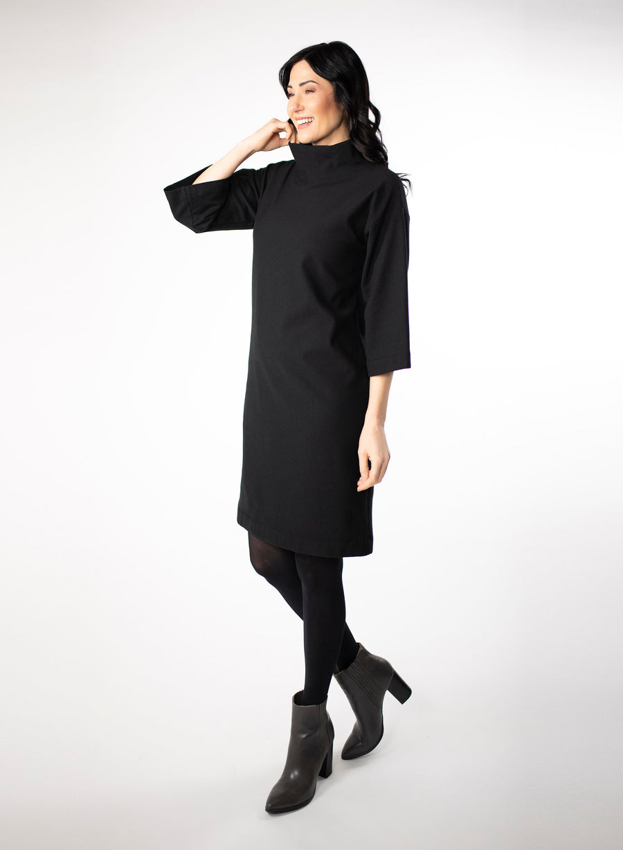 Black knee length Bamboo fleece sweater dress with full sleeves and wide mock neck collar. Styled with black leggings.