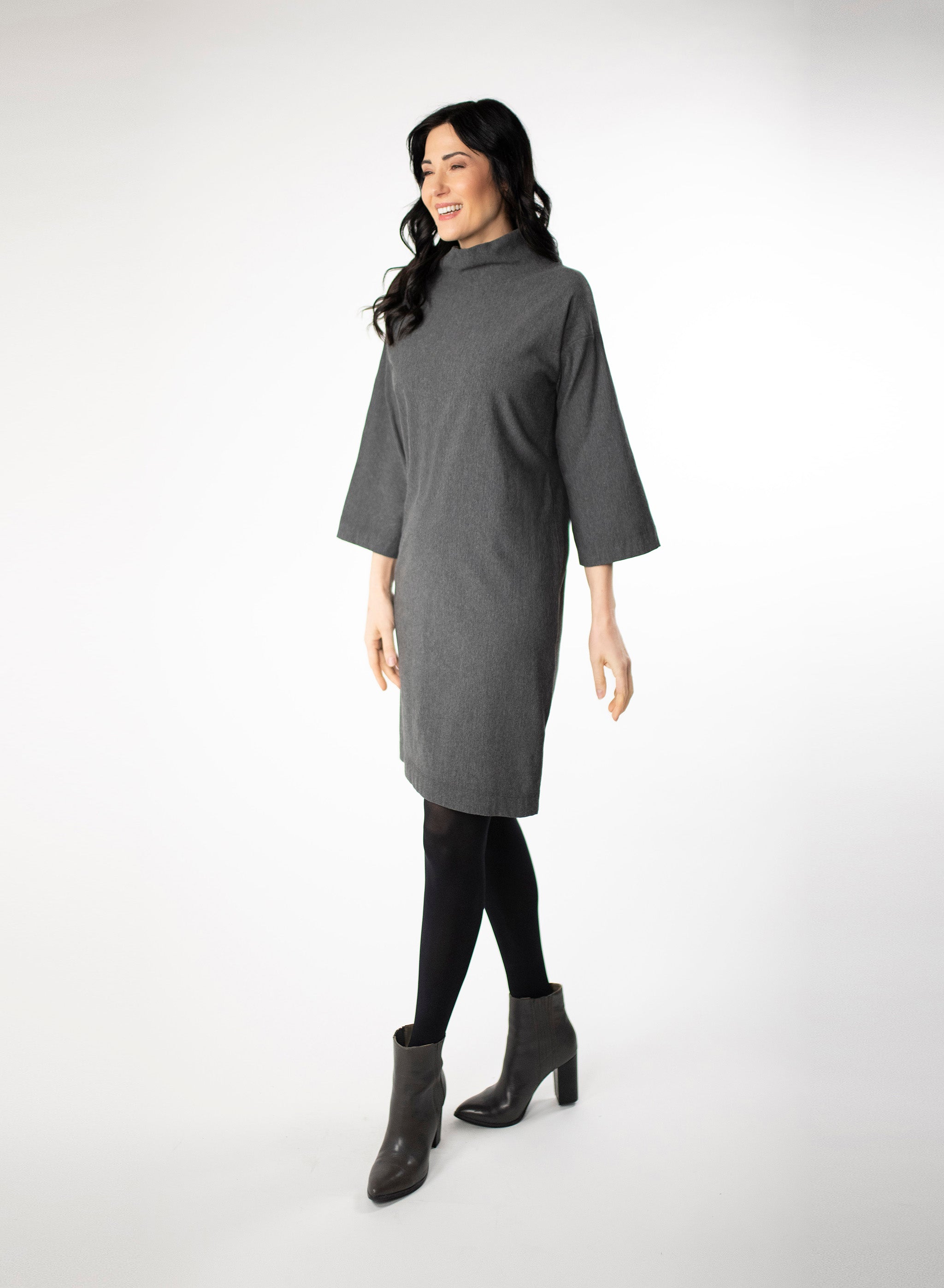 Charcoal Grey knee length Bamboo fleece sweater dress with full sleeves and wide mock neck collar. Styled with black leggings.