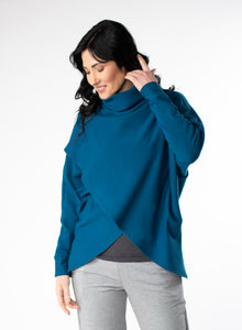 Blue fleece sweater with cowl neck and dolman cuffed sleeves. Sweater features a reverse-V drape in front. Styled with grey tank base layer