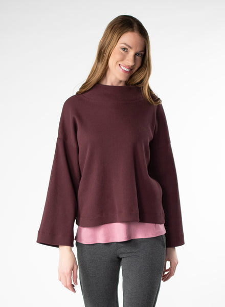 Plum waffle knit cropped sweater. Wide mock neck style neckband and full sleeves. Styled with pink mock neck under and charcoal leggings.