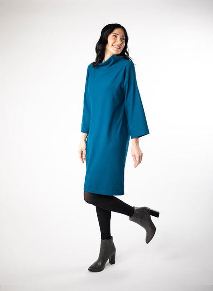 Blue knee length Bamboo fleece sweater dress with full sleeves and wide mock neck collar. Styled with black leggings. 