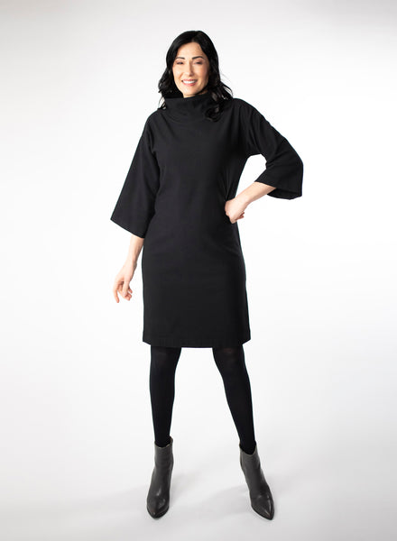 Black knee length Bamboo fleece sweater dress with full sleeves and wide mock neck collar. Styled with black leggings. 