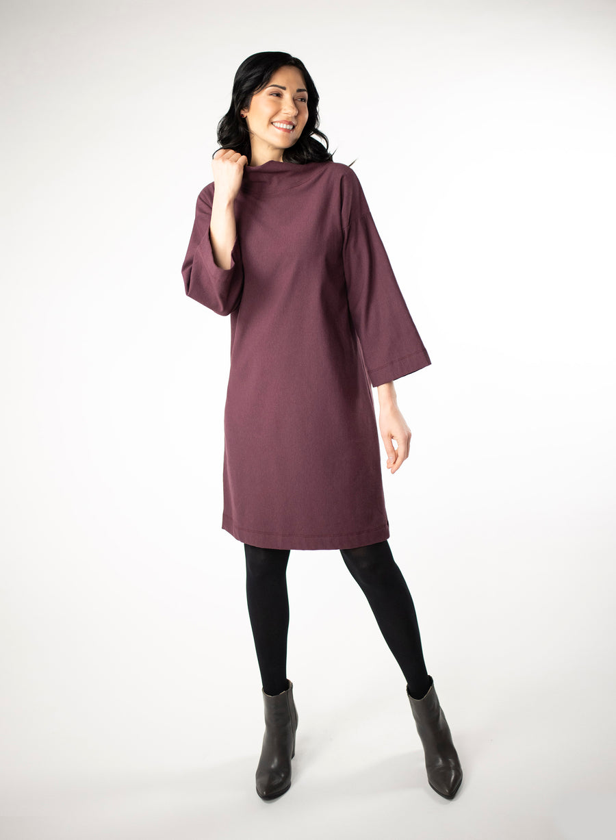 Plum knee length Bamboo fleece sweater dress with full sleeves and wide mock neck collar. Styled with black leggings. 