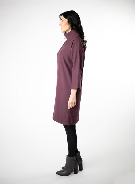 Plum knee length Bamboo fleece sweater dress with full sleeves and wide mock neck collar. Styled with black leggings. 