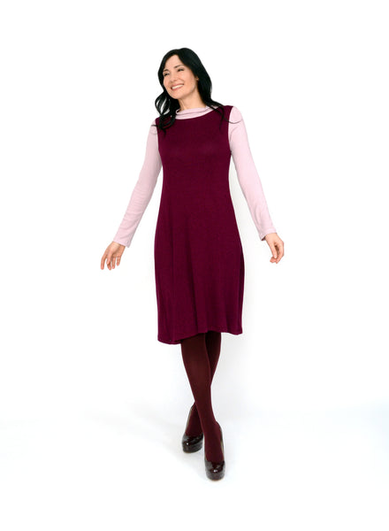 Burgundy reversible neckline tank dress. Two-way neckline showing the boat neck in front. Dress length ends below the knee. Styled with light pink ribbed mock neck under.