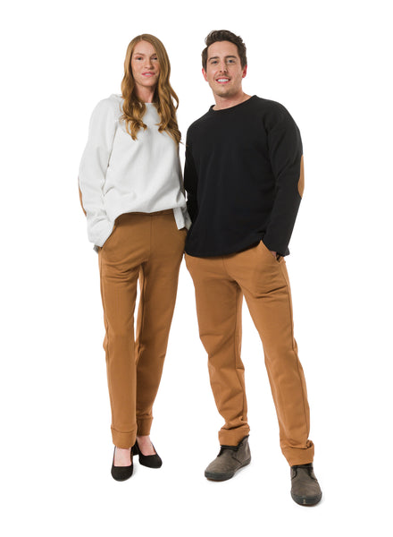 Model 1: Off-White Cream unisex sweater with nutmeg elbow patch. Model 2: Black unisex sweater with nutmeg elbow patches. Both styled with Nutmeg unisex trousers